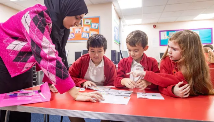 A tutor listens as three young pupils share some work