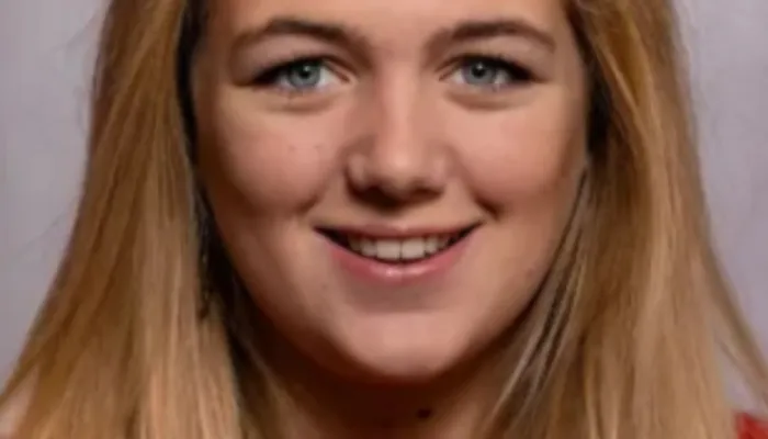 penny smiles into the camera in a red jumper