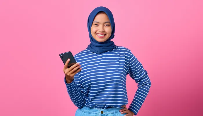 a young woman holds a mobile phone, smiling on a vivid pink background
