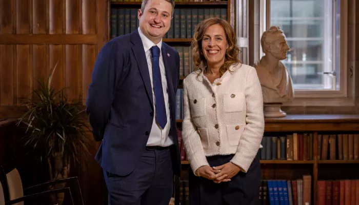 A man and a woman, standing in front of a bookcase, smile to the camera.