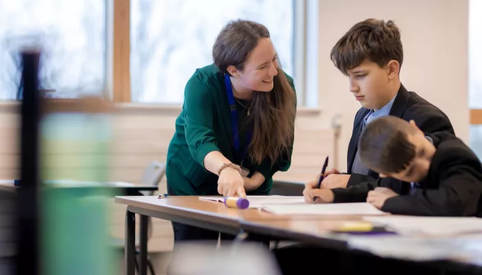 A female tutor is smiling at two pupils as they tackle a Maths problem. 