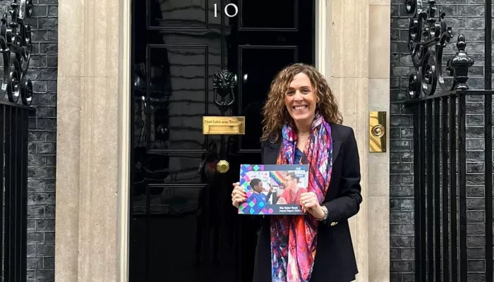 Abigail stands outside the distinctive door of Number 10 Downing Street, holding a copy of the Tutor Trust's 2022 Impact Report