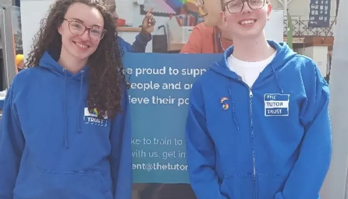 The Tutor Trust team, wearing blue, branded sweat tops. smile in front of our Pride banner
