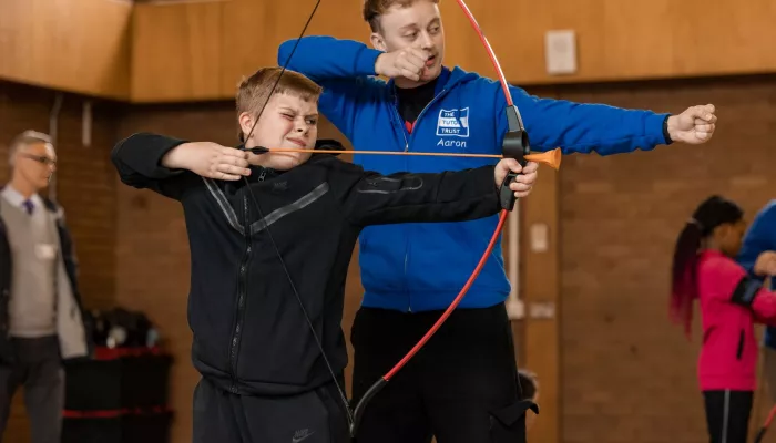 A tutor and a pupil prepare to fire a bow and arrow during a fun activity at an Easter Club