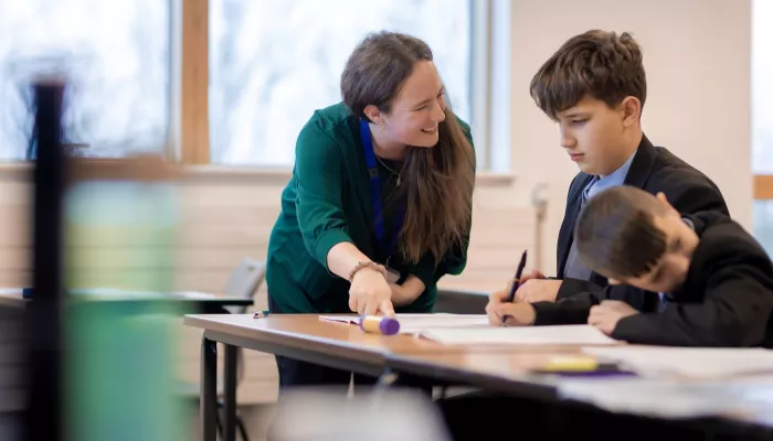 A tutor smiles at a pupil as she points out some content in an exercise book