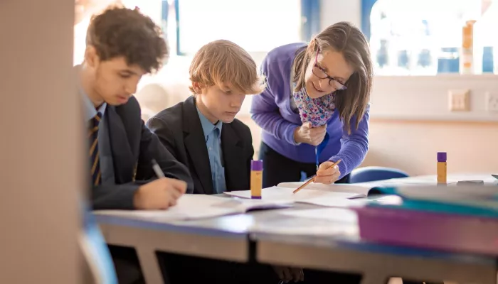 A tutor wearing  lilac jumper supports two students in a Maths session