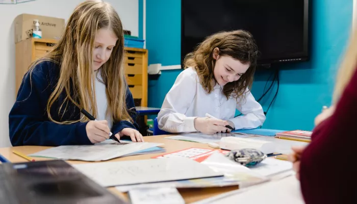 Two pupils are smiling as they write in exercise books