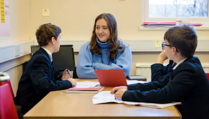 A tutor, wearing a blue jumper, is talking to two pupils in a session