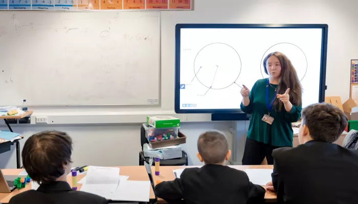 A tutor stands at a whiteboard in front of a group of three pupils.