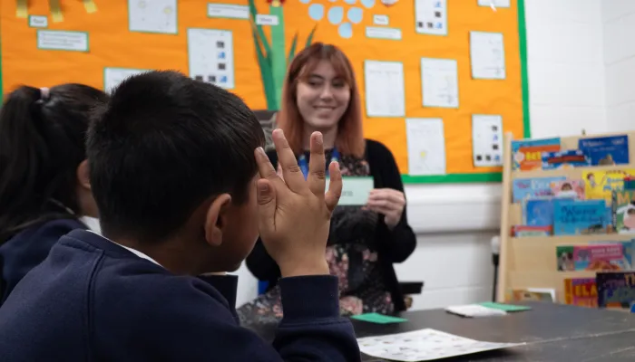 A pupil raises his hand to pronounce a phonics card which is held up by a tutor