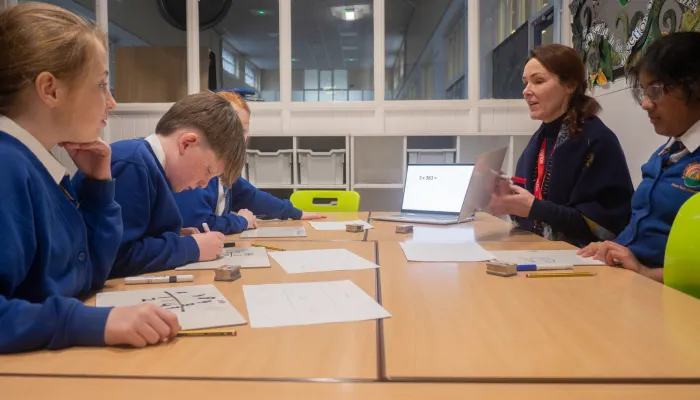 Four year six pupils in blue school uniforms sat at a table. They are taking part in a small-group tuition session in a primary school.