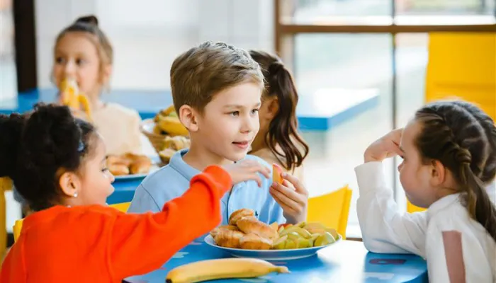 Children in school uniform sat around a small table eating lunch