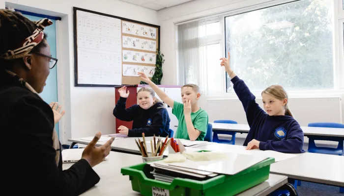 Year 5 pupils raise their hands in a small group tutoring session