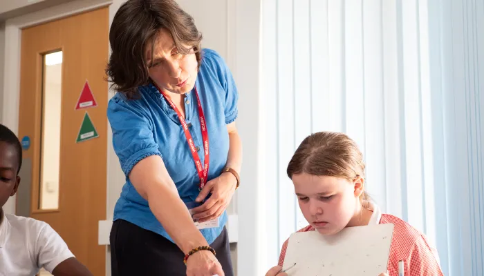 a female tutor works with a young pupil in a pink top
