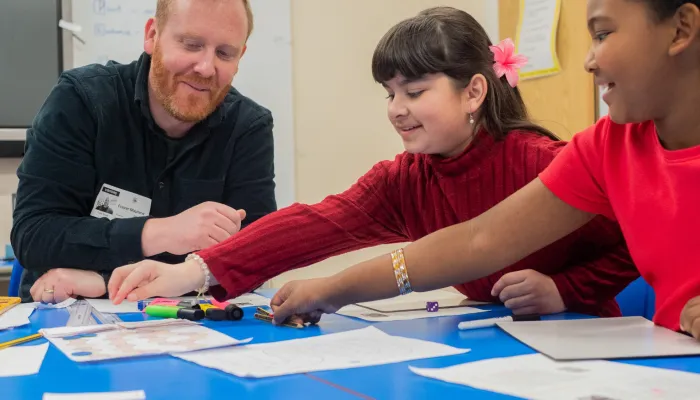 A male tutor delivers reading lessons to two primary pupils