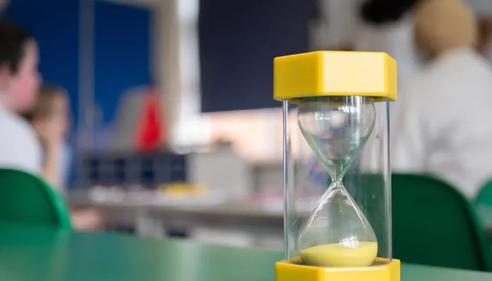 A yellow sand timer on a green classroom table.