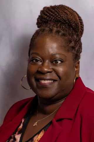 Deborah ensures our offices run smoothly and are welcoming places to work. She has dark brown hair in a bun and is wearing a red jacket.