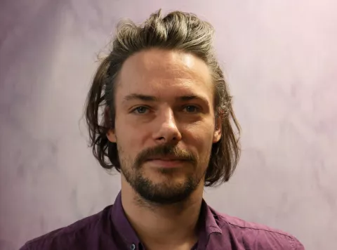 Will is a keen advocate of social mobility, and uses his role to help students from backgrounds similar to our tutees, to have the opportunity to tutor with us, Will is dark-haired with a beard and moustache. He is wearing a burgundy shirt.