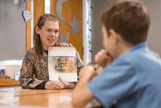 A tutor holds up an image and is speaking to a pupil