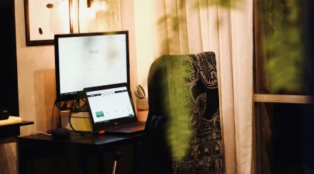 a desk with computer screens and a chair with a shawl represent a home office