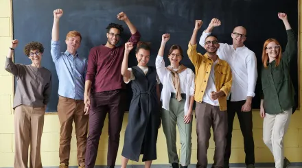 four men and two women raise a celebratory hand in front of a chalkboard