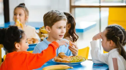 Children in school uniform sat around a small table eating lunch