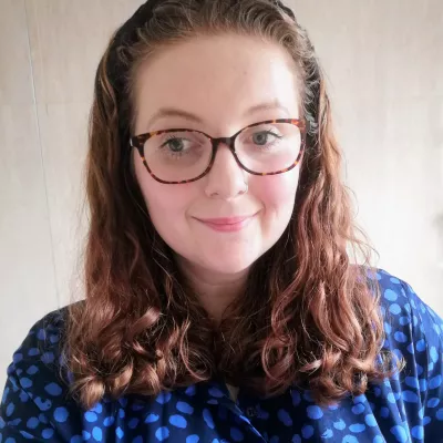 Fran is keen to dismantle barriers to learning for pupils. Fran has shoulder-length brown hair, is wearing a blue dress and has glasses.