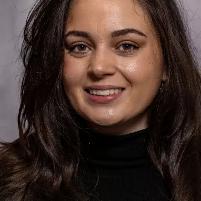 Hannah Cunningham is a former teacher who enjoys making a positive impact on young people's lives.  Hannah has long brown hair and is wearing a black jumper.