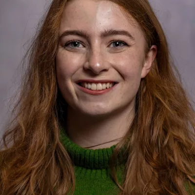 Lauren uses data to help us recruit those individuals who share our values and will deliver high-quality tuition. Lauren has long auburn hair and is wearing a green turtle neck woollen jumper.