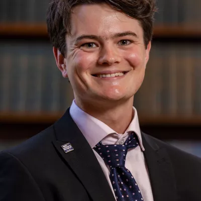 Theo, a former tutor, now ensures more young people, like him, can take up the opportunity. He is wearing a white shirt, with a tie and jacket.