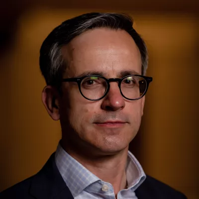 A man wearing glasses looks at the camera. He is wearing an open-necked shirt.