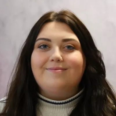 Keira is passionate about interrogating our data and finding out how we can continue to improve. Keira has long brown hair and is wearing a khaki coloured top.