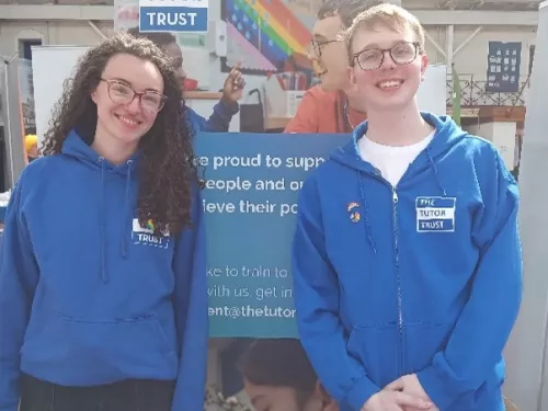 The Tutor Trust team, wearing blue, branded sweat tops. smile in front of our Pride banner