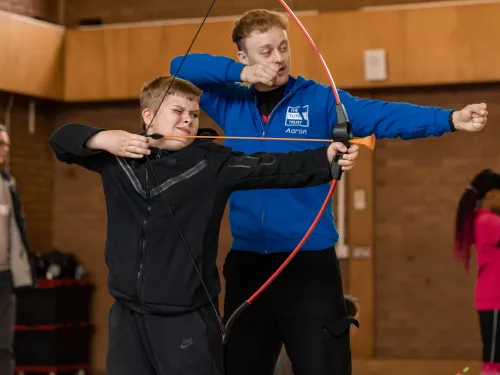 A tutor and a pupil prepare to fire a bow and arrow during a fun activity at an Easter Club