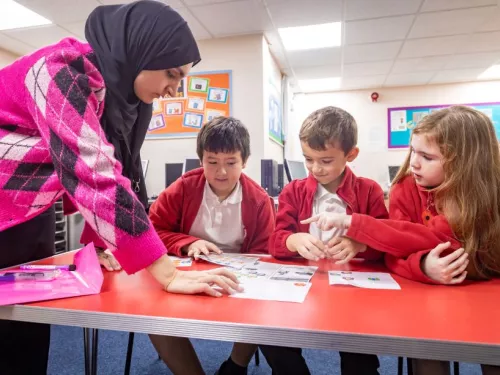 A tutor listens as three young pupils share some work