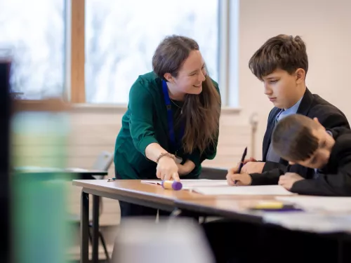 A tutor smiles at a pupil as she points out some content in an exercise book
