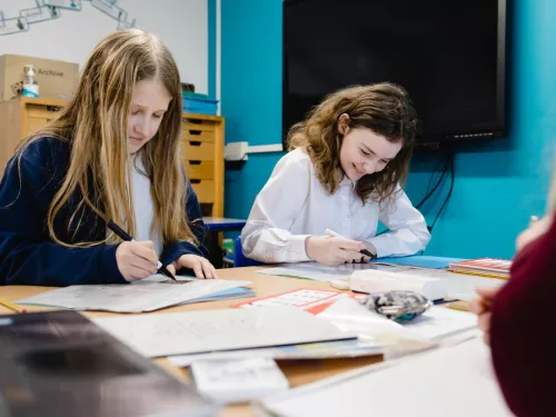 Two pupils are smiling as they write in exercise books
