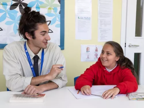 A tutor and pupil are smiling during a reading tuition session