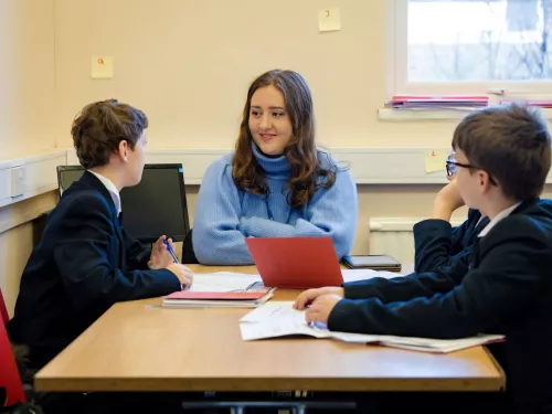 A tutor, wearing a blue jumper, is talking to two pupils in a session