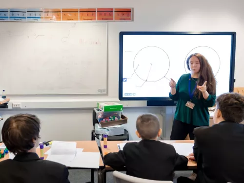 A tutor stands at a whiteboard in front of a group of three pupils.