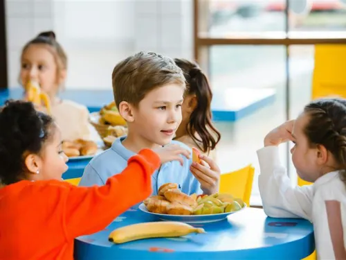Children in school uniform sat around a small table eating lunch