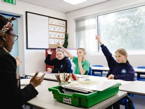 Year 5 pupils raise their hands in a small group tutoring session