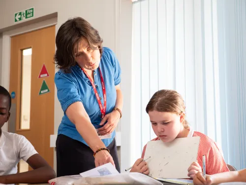 a female tutor works with a young pupil in a pink top