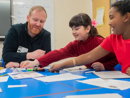 A male tutor delivers reading lessons to two primary pupils